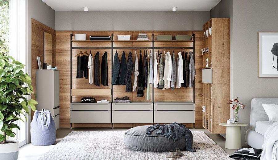 Modernes Ankleidezimmer mit offenem Regalsystem in Holzoptik, hängender Kleidung, Schubladen und seitlicher Stauraumlösung.