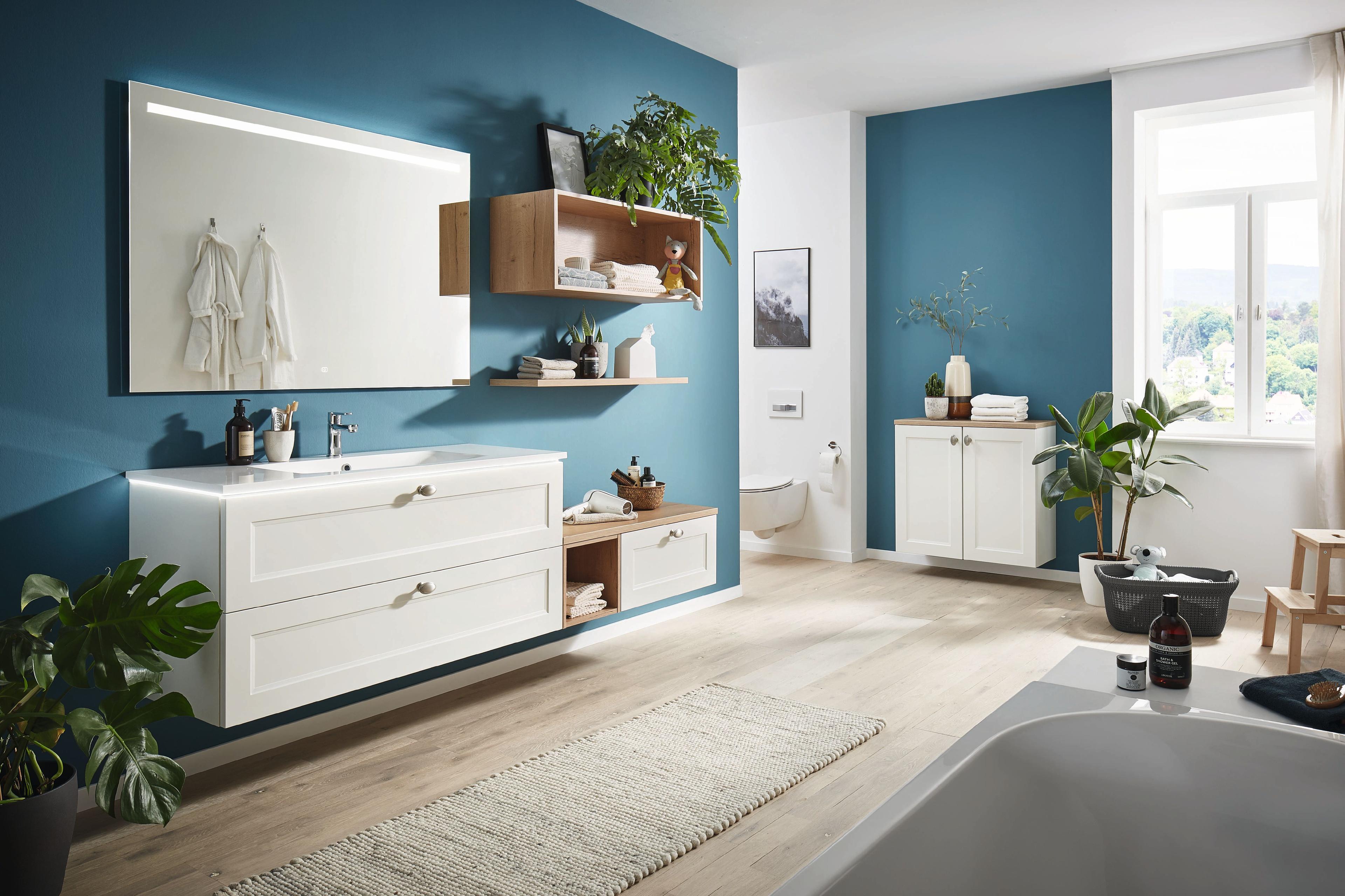 Helles Badezimmer mit weißem Waschtischunterschrank, großer Spiegelfläche, offenen Holzregalen und blauer Wandgestaltung.
