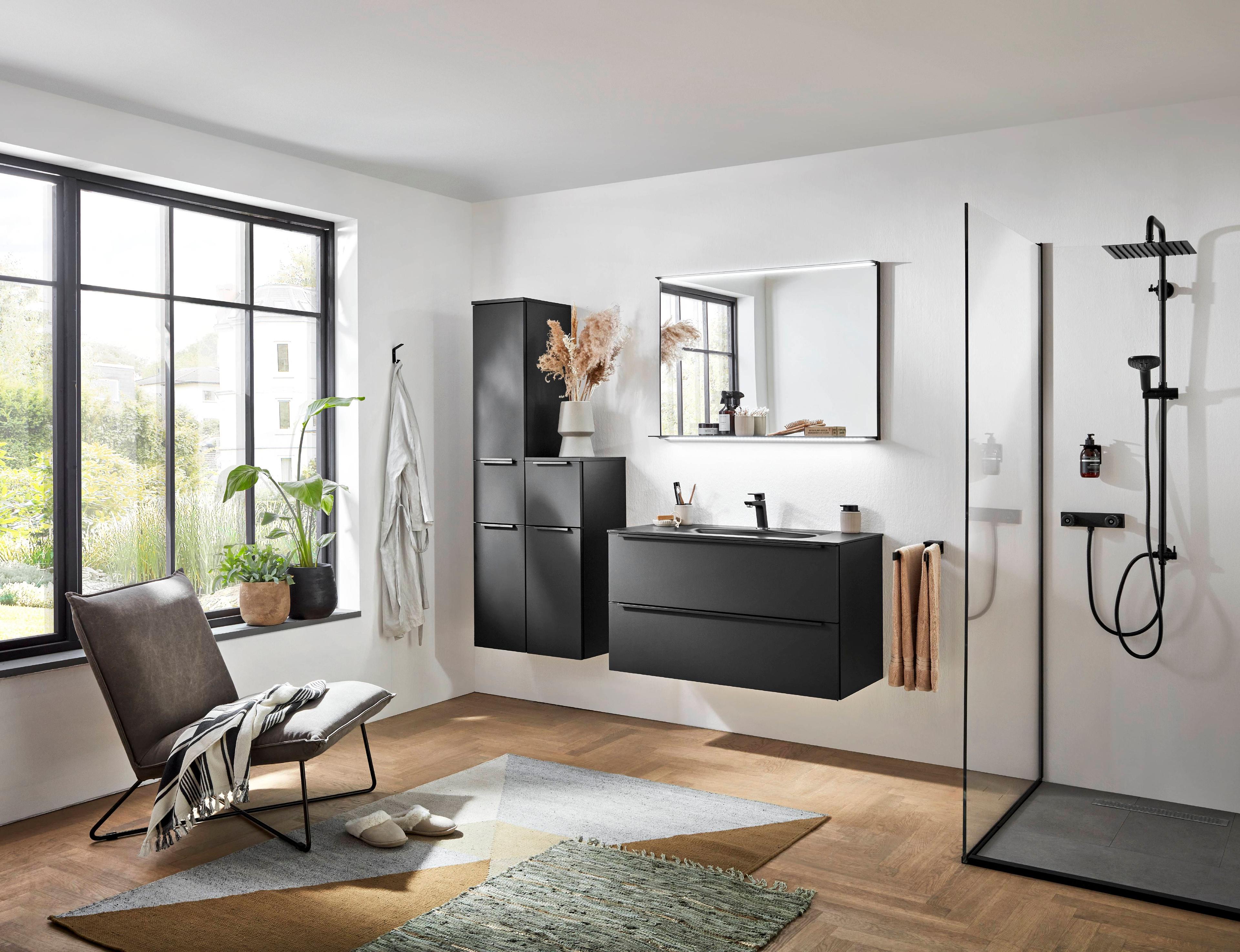 Modernes Badezimmer mit schwarzen Badmöbeln, bodengleicher Dusche, großem Fenster und gemütlicher Sitzgelegenheit auf Parkettboden.
