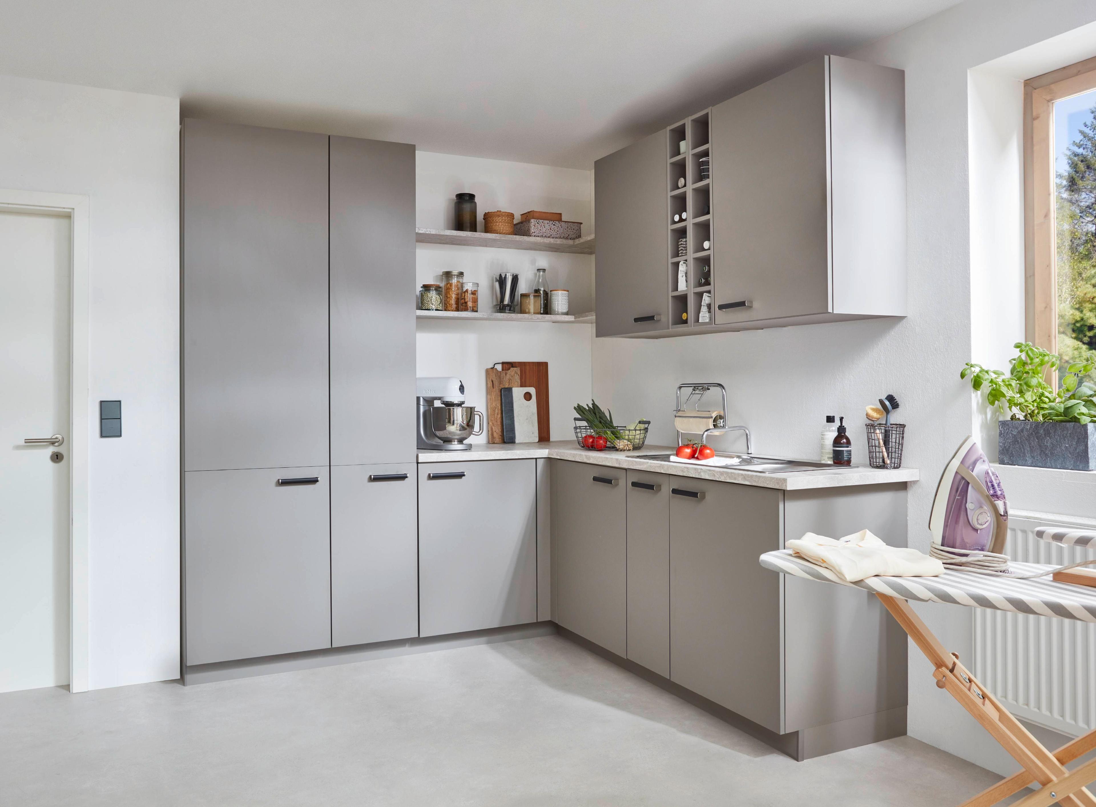 Moderner L-förmiger Hauswirtschaftsraum in Grau mit weißer Arbeitsplatte, offenen Regalen, Küchengeräten und einem Bügelbrett am Fenster.