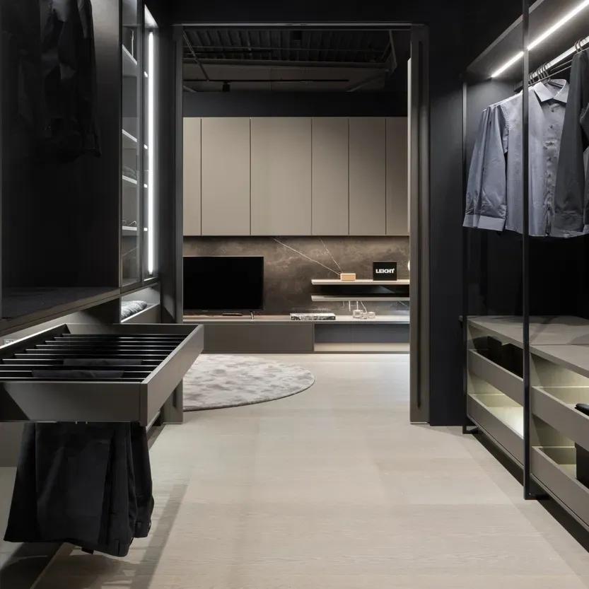 Ankleidebereich in dunklem Design mit praktischen Auszügen, Hosenhalter und Durchgang zu einem modernen Wohnbereich mit TV-Möbel.