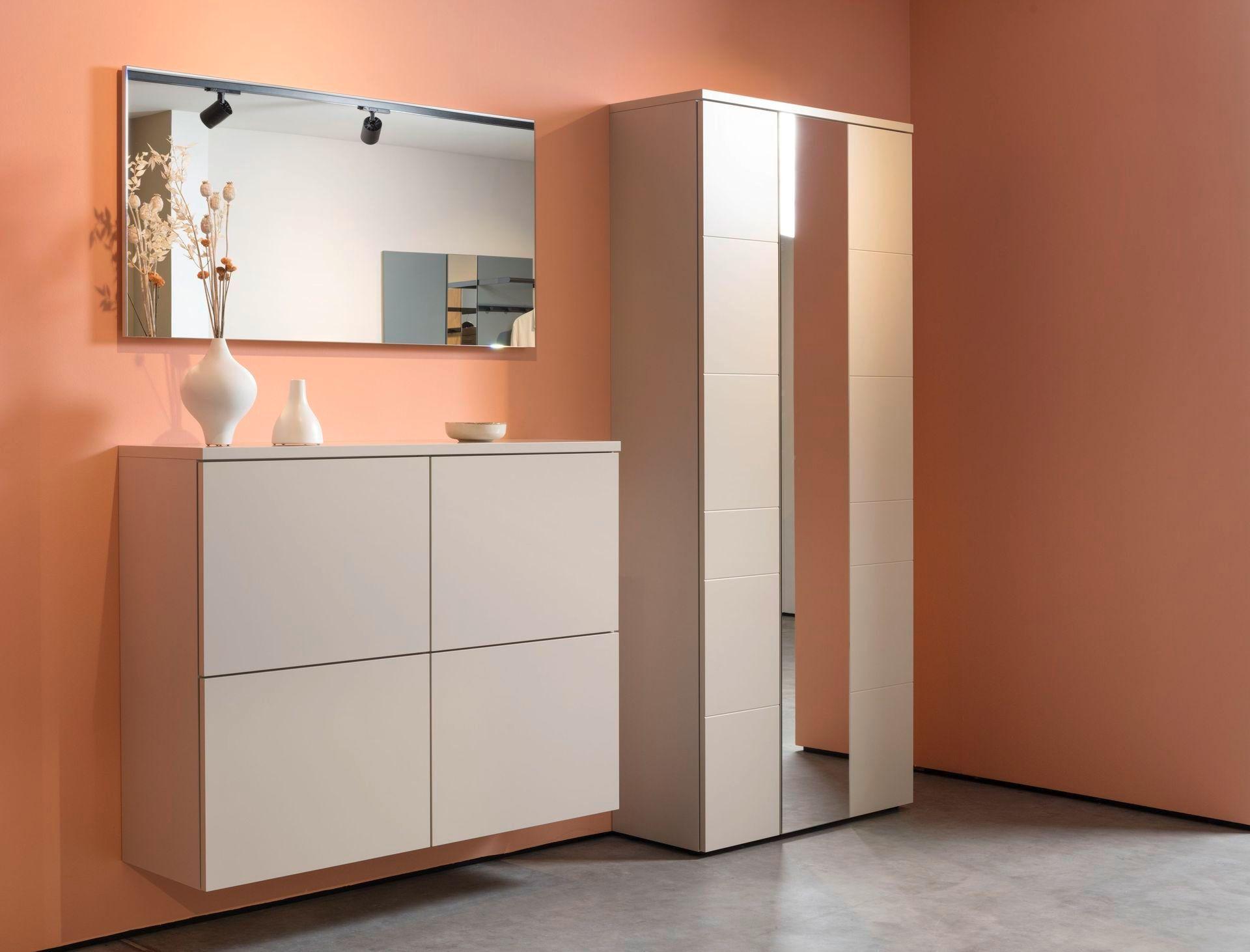 Wandhängende Garderobenkommode und Spiegelschrank in Creme vor apricotfarbener Wand.