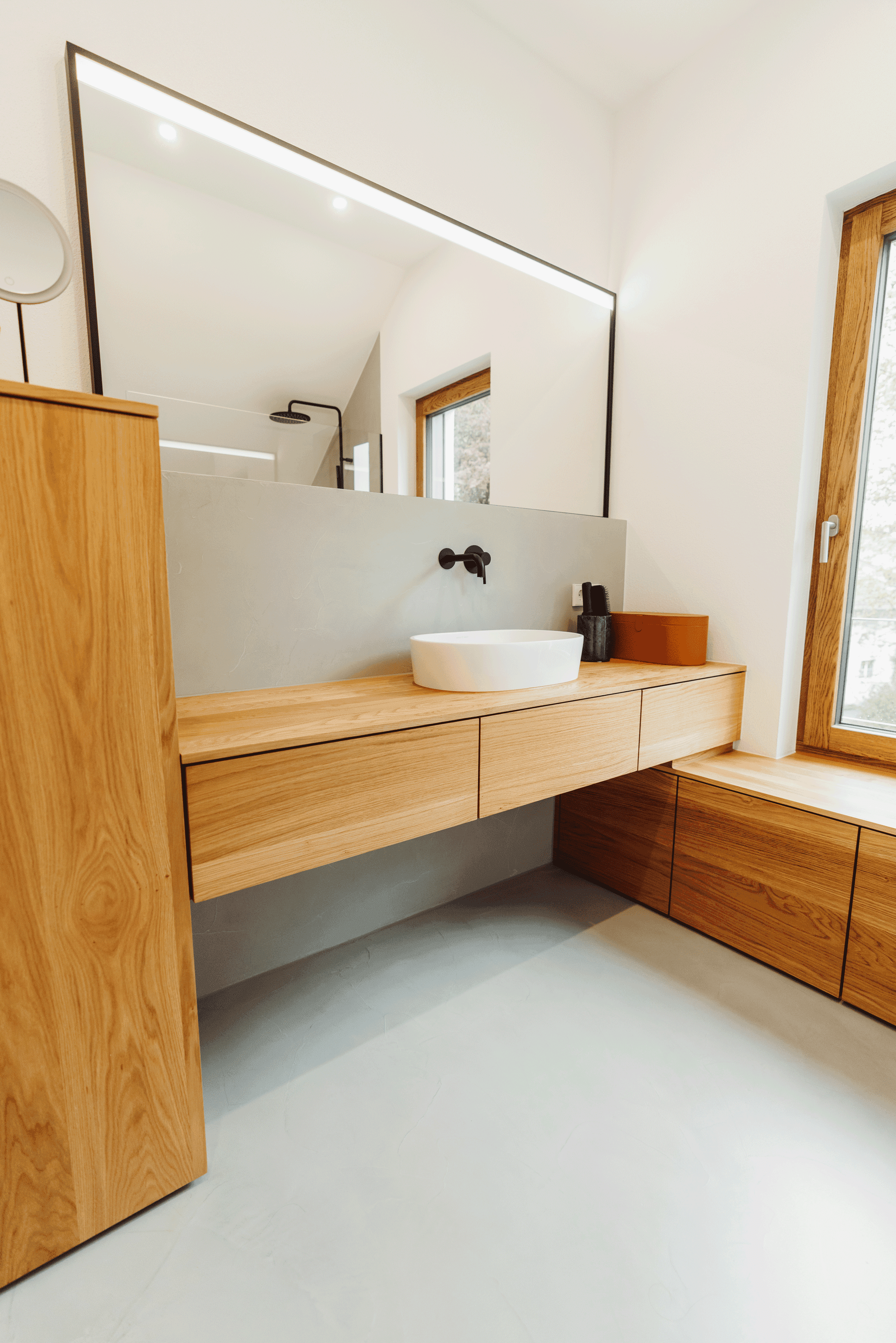 Modernes Badezimmer mit schwimmenden Holzmöbeln, weißem Aufsatzwaschbecken, schwarzer Wandarmatur und großem Spiegel mit LED-Beleuchtung.