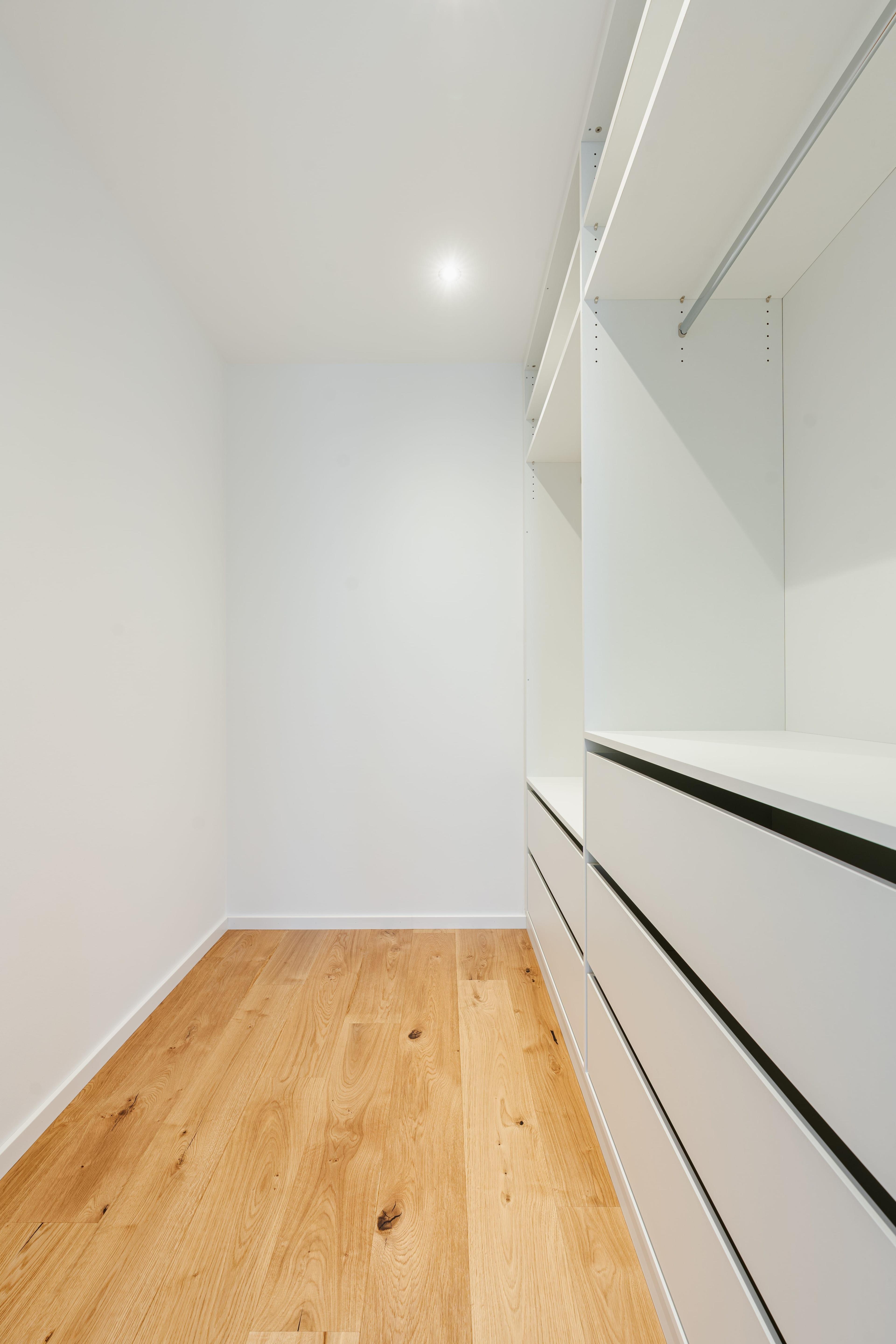 Schlichtes, modernes Ankleidezimmer mit weißen Einbaumöbeln und Eichenboden – individuell umgesetzt von der Schreinerei Möbel Grell.