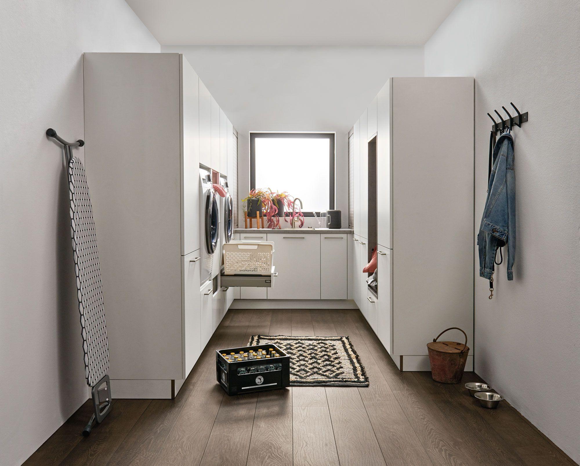 Heller Hauswirtschaftsraum mit weißen Hochschränken, integrierter Waschmaschine, praktischen Wandhaken und warmem Holzboden für optimale Organisation.