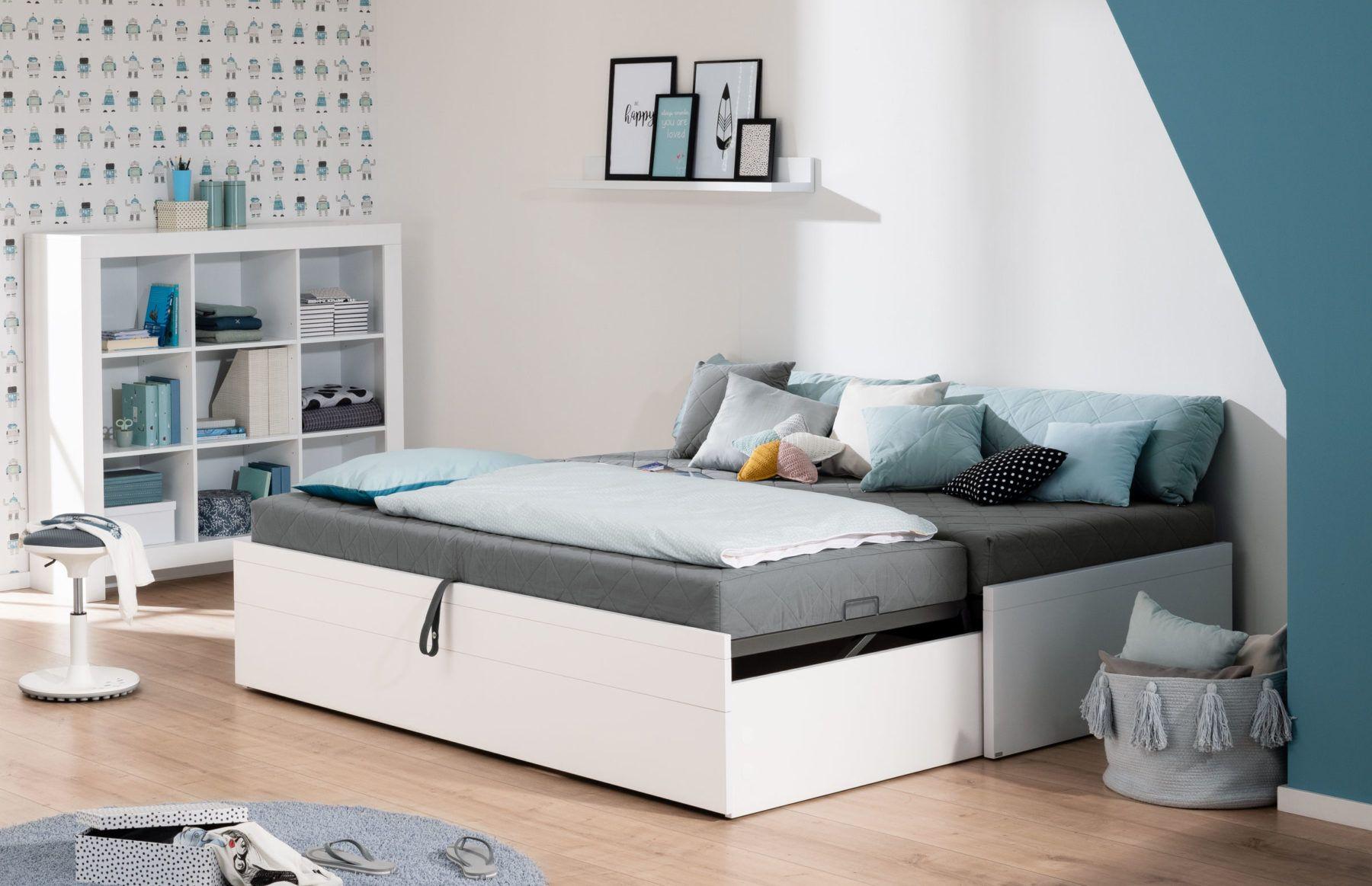 Gemütliches Kinderzimmer mit weißem Doppelbett inklusive Ausziehfunktion, vielen Kissen und offener Regalwand – in sanften Blau- und Grautönen gestaltet.