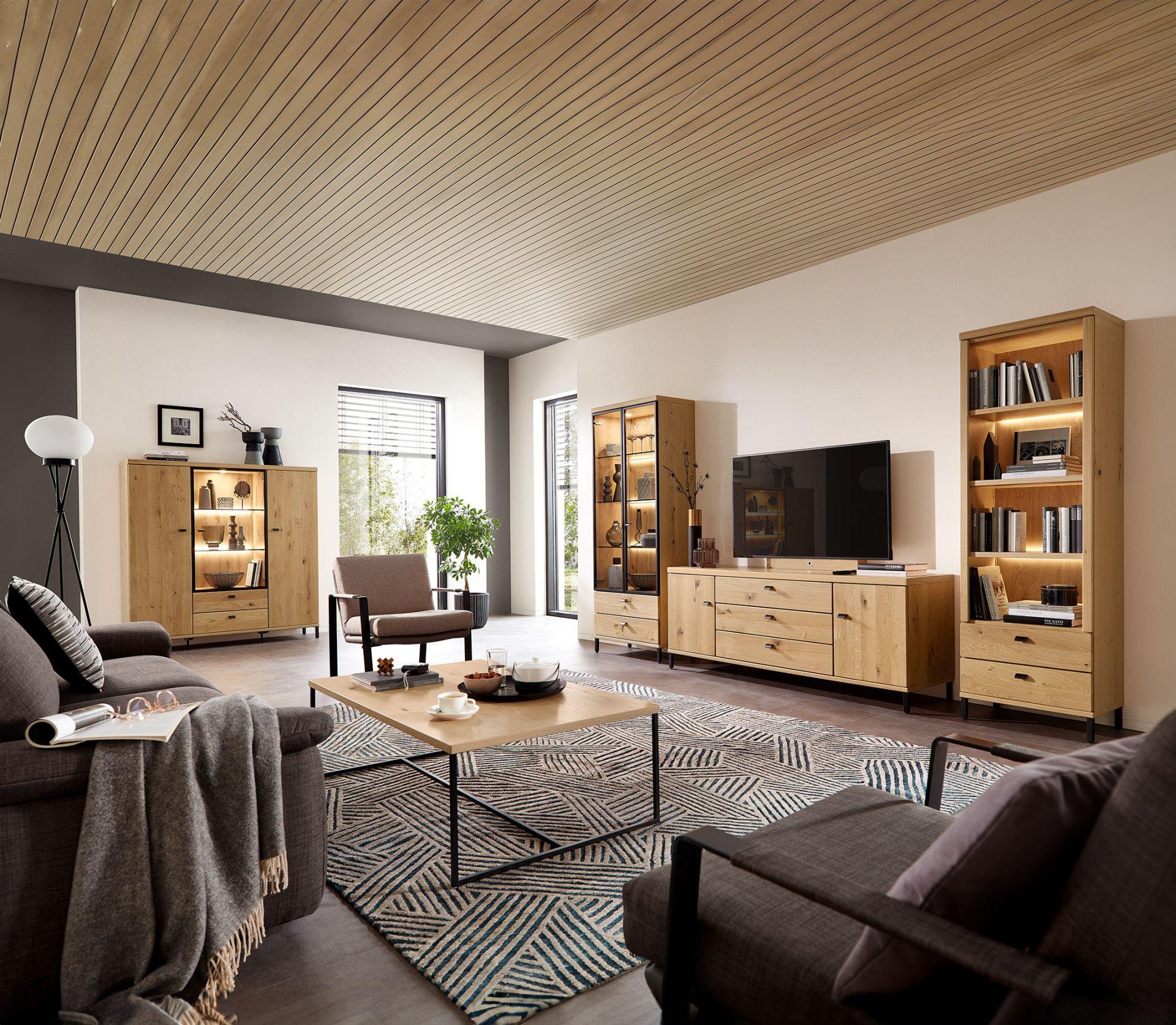 Gemütlich eingerichtetes Wohnzimmer mit Wohnwand, Vitrinen, Bücherregal und Couchtisch in Asteiche – kombiniert mit dunklen Polstermöbeln und modernem Dekor.