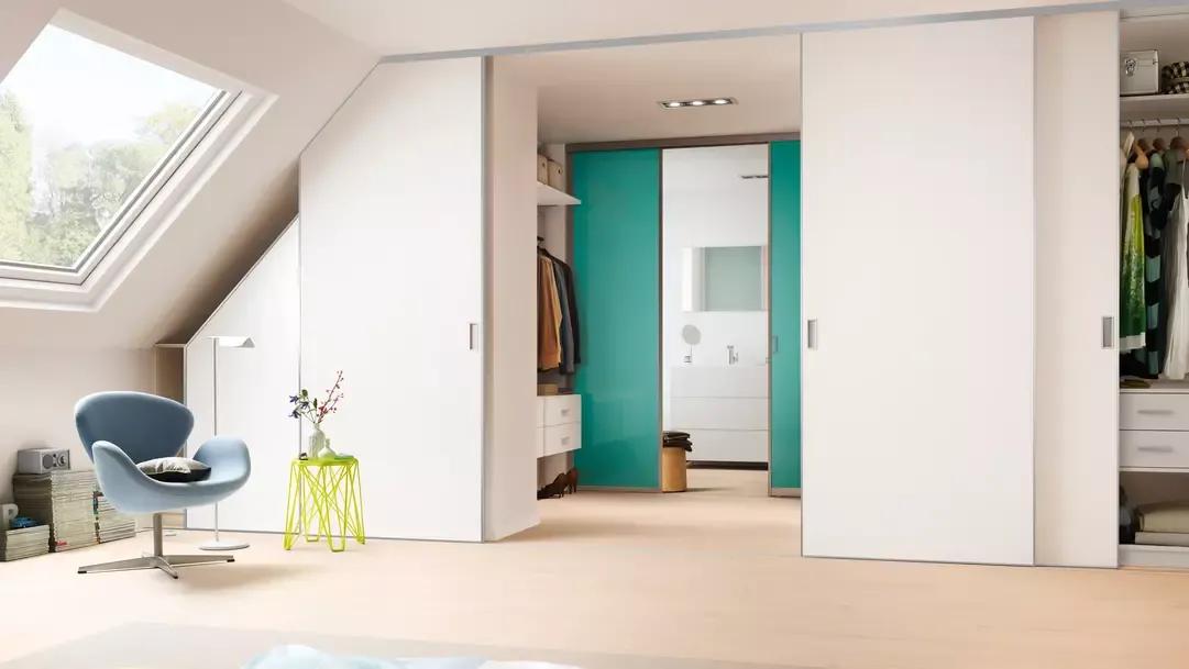 Modernes Ankleidezimmer unter der Dachschräge mit weißen Schiebetüren, türkisfarbenem Durchgang zum Badezimmer und integriertem Stauraum.