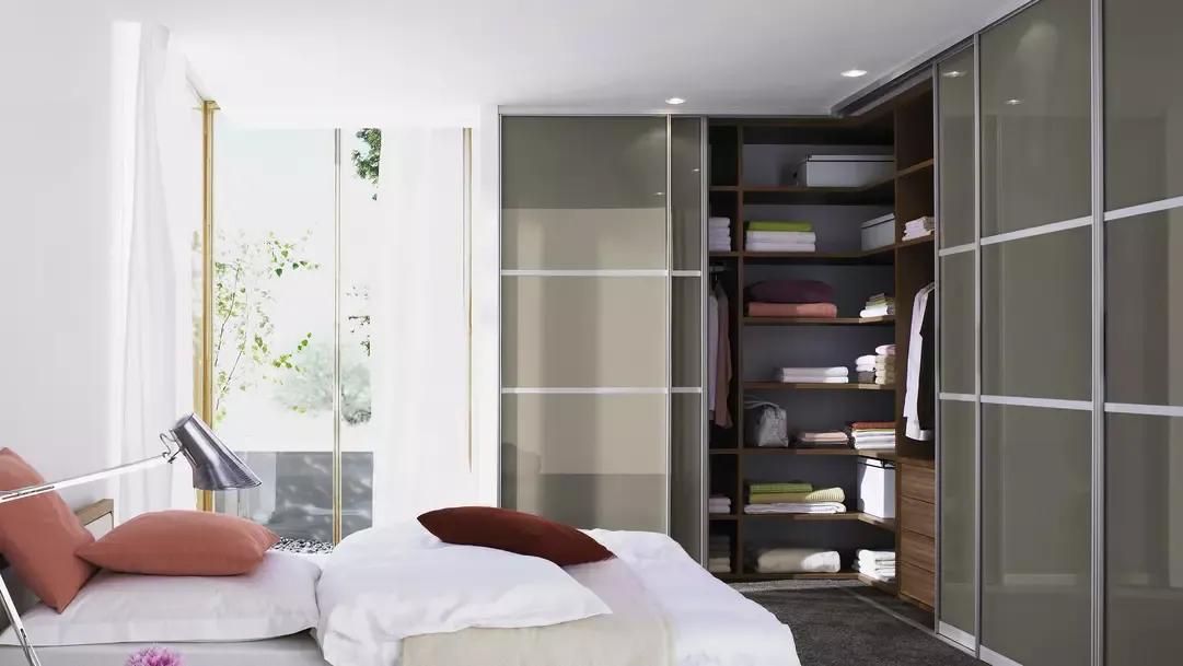 Begehbarer Kleiderschrank mit Schiebetüren und offener Regallösung in einem hellen, lichtdurchfluteten Schlafzimmer mit modernen Akzenten.