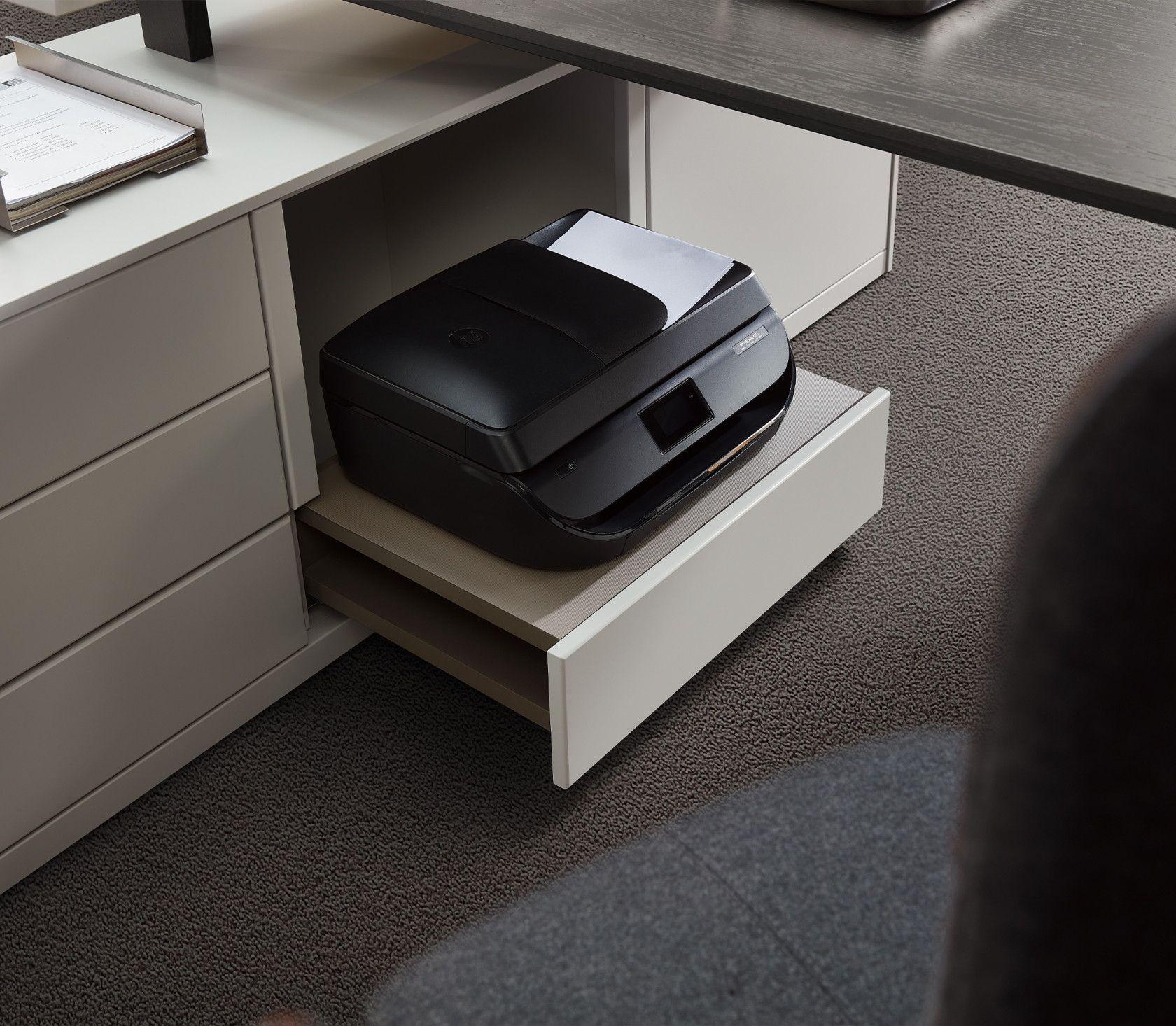 Multifunktionsdrucker steht auf einer ausziehbaren weißen Schublade unter einem Schreibtisch - praktische platzsparende Lösung für das Büro.