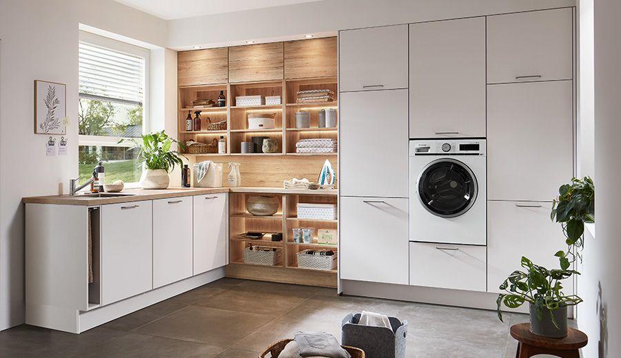 L-förmiger Hauswirtschaftsraum in Weiß-Holz-Kombination mit offenen Regalen, integrierter Waschmaschine und viel Tageslicht.