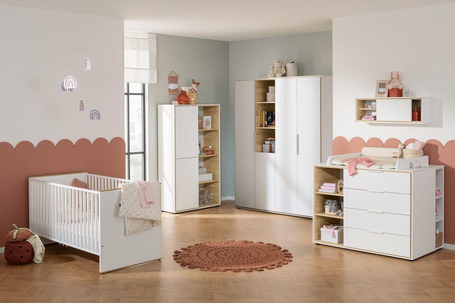 Helles Babyzimmer mit weißem Gitterbett, Wickelkommode, Kleiderschrank und Regalen in Holz-Weiß-Kombination – liebevoll dekoriert in Rosa- und Naturtönen.
