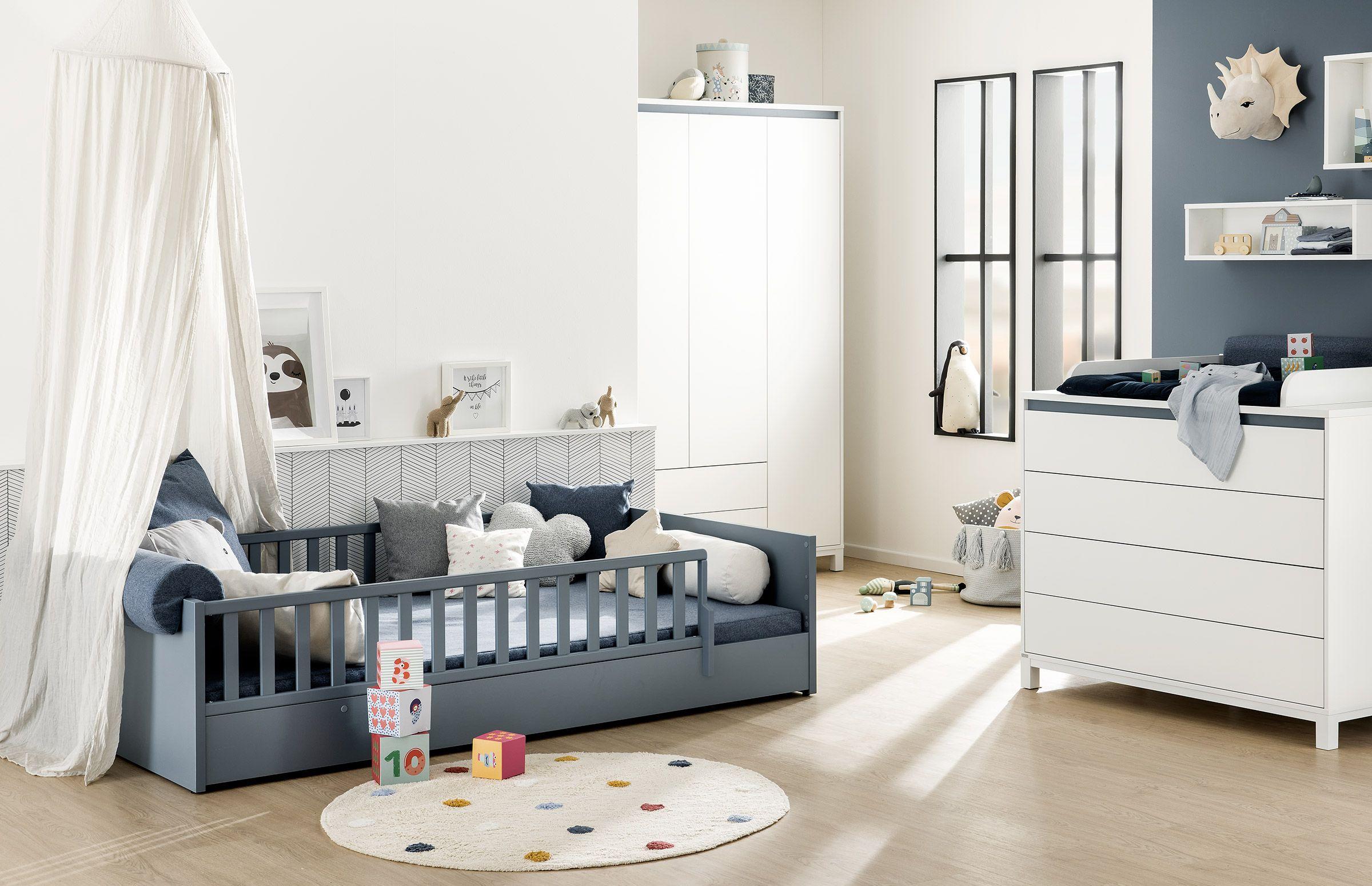 Modernes Babyzimmer mit dunkelblauem Gitterbett, Wickelkommode, weißem Kleiderschrank und spielerischer Deko – freundlich und funktional eingerichtet in Blau-Weiß-Tönen.