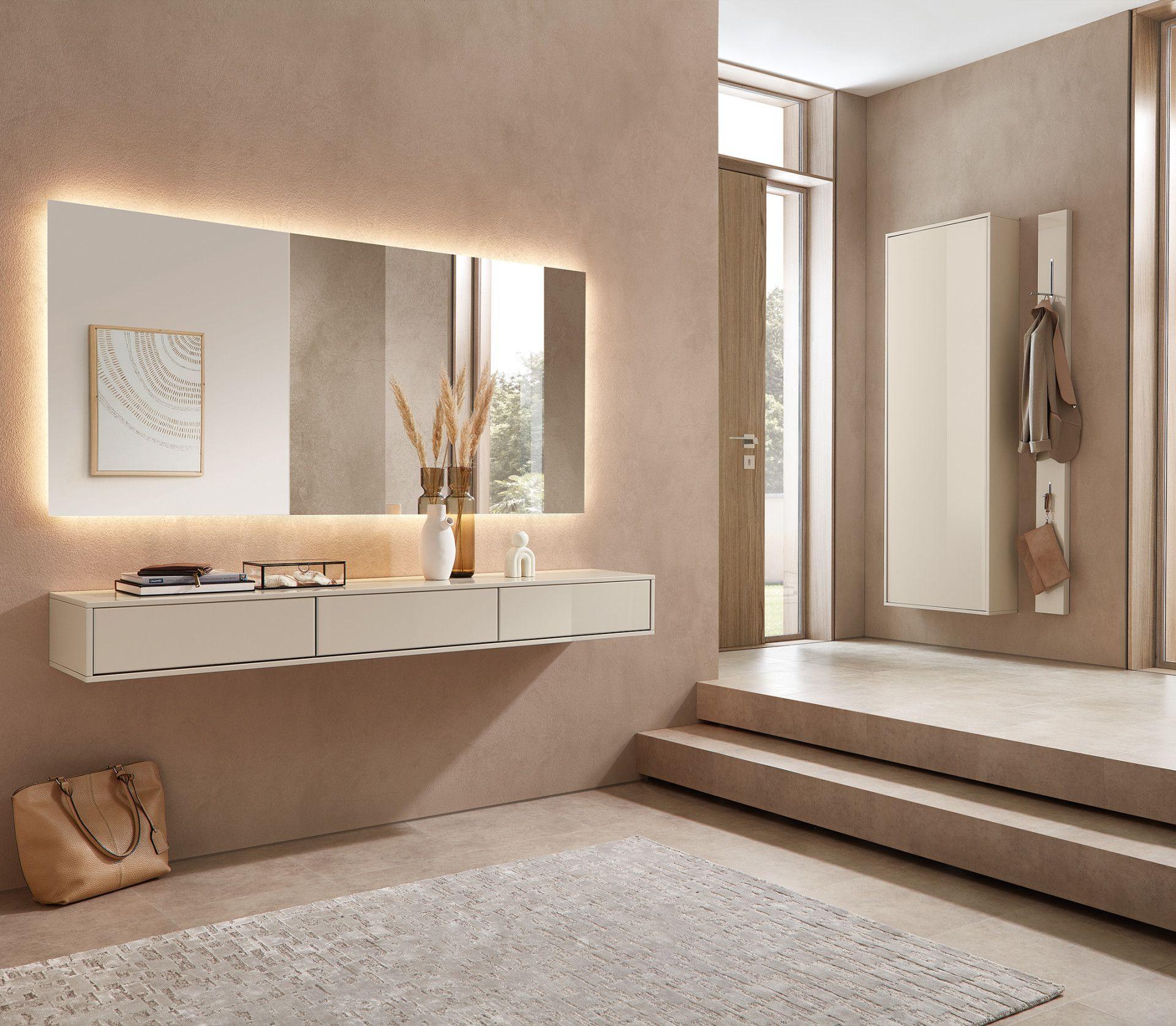 Moderne Garderobe in Creme mit beleuchtetem Wandspiegel, schwebender Kommode und Hakenleiste in einem stilvoll eingerichteten Flur mit natürlichem Lichteinfall.