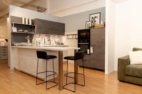 Moderne Küche mit weißer Kücheninsel, anthrazitfarbenen Oberschränken und hellen Unterschränken. Zwei schwarze Barhocker vor der Insel, Fliesenspiegel mit Stadtmotiv und offene Regale mit Dekoration.