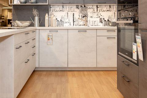 Moderne Küche mit weißer Kücheninsel, anthrazitfarbenen Oberschränken und hellen Unterschränken. Zwei schwarze Barhocker vor der Insel, Fliesenspiegel mit Stadtmotiv und offene Regale mit Dekoration.