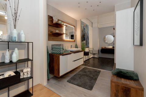 Luxuriöse Badausstellung mit weißem Waschtisch-Unterschrank, Nussbaum-Elementen, beleuchtetem Spiegelschrank und modernen Accessoires.