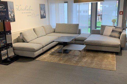 Große graue Stoff-Wohnlandschaft in U-Form mit schwarzem Couchtisch unter industrieller Holzbalkendecke.