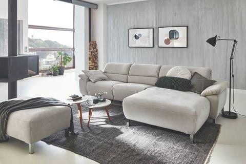 Hellgraue Eckcouch mit Chaiselongue und Holz-Couchtisch auf rosa Hochflor-Teppich in Möbelhaus-Showroom.