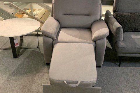 Klassischer grauer Sessel mit gepolsterten Armlehnen zwischen anderen Sitzmöbeln in Showroom.