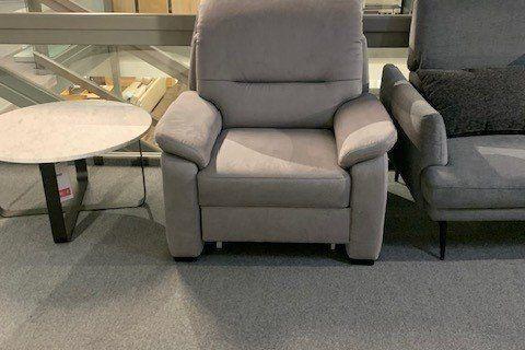 Klassischer grauer Sessel mit gepolsterten Armlehnen zwischen anderen Sitzmöbeln in Showroom.